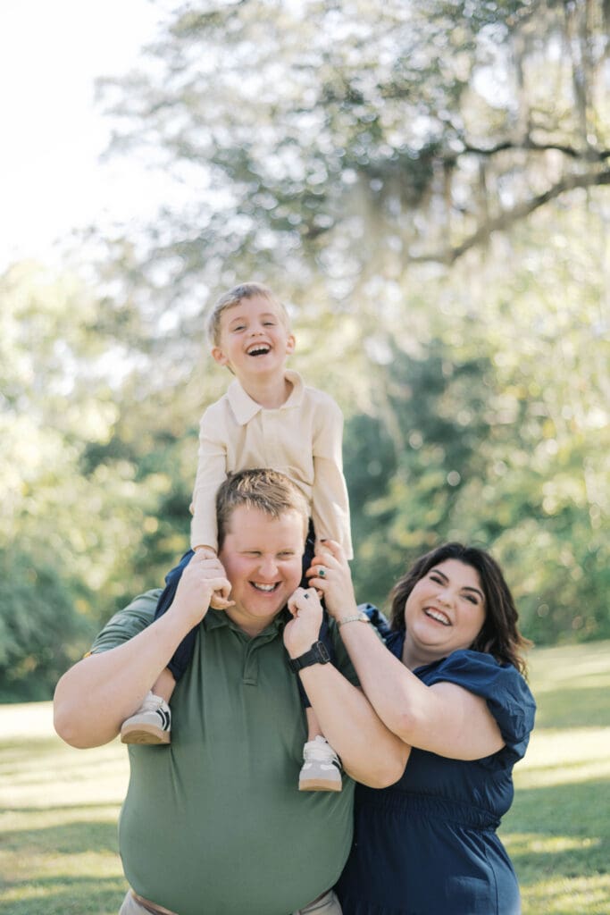 Boy laughs while looking at the camera while riding on Dad's shoulders