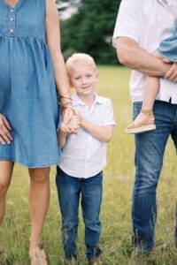 A close up image of a blonde hair boy dressed in denim smiling at the camera