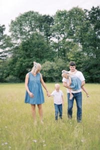 A family of four dressed in denim walk through a field of tall grass and flowers