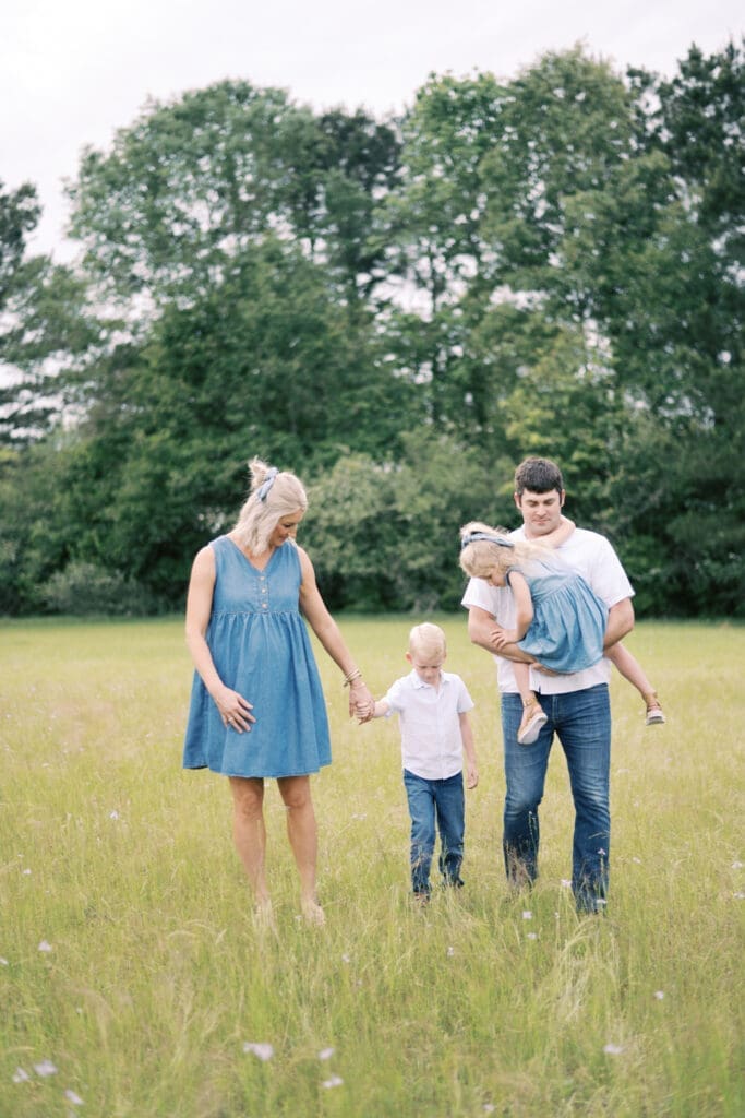 A family of four dressed in denim walk through a field of tall grass and flowers