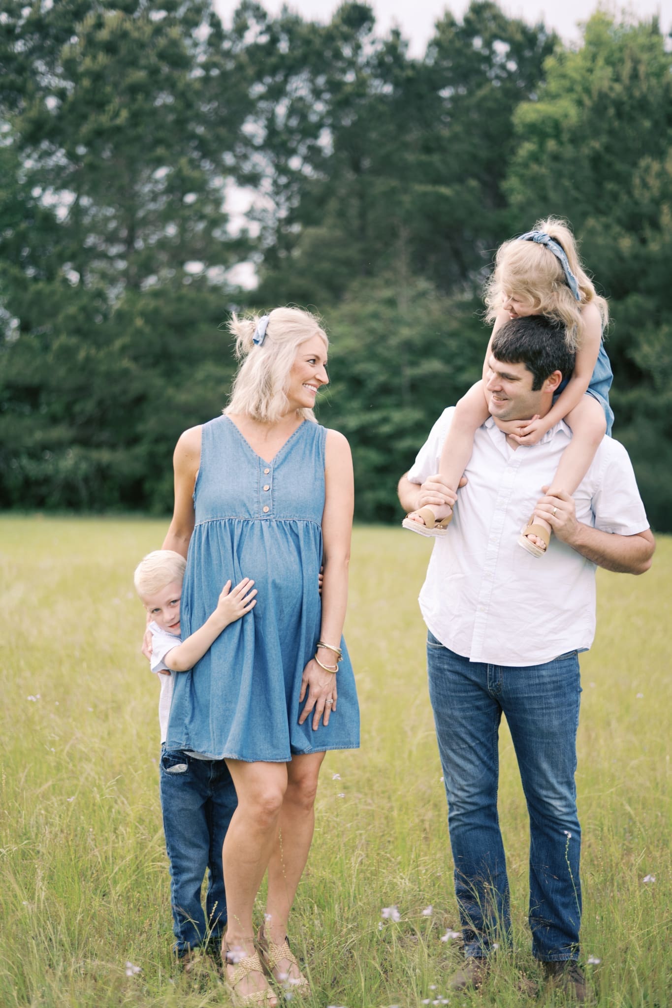 A family of four dressed in denim looks at each other and smiles as they walk through a field of tall grass and flowers in the Baton Rouge area