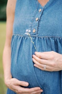A close up image of a pregnant mother as she holds a flower in front of her baby bump