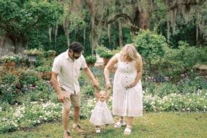 A mom and dad swing their toddler in the air with flowers in the background