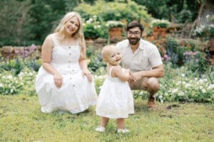 A toddler looks over her shoulder and smiles at the camera while the parents look lovingly at her
