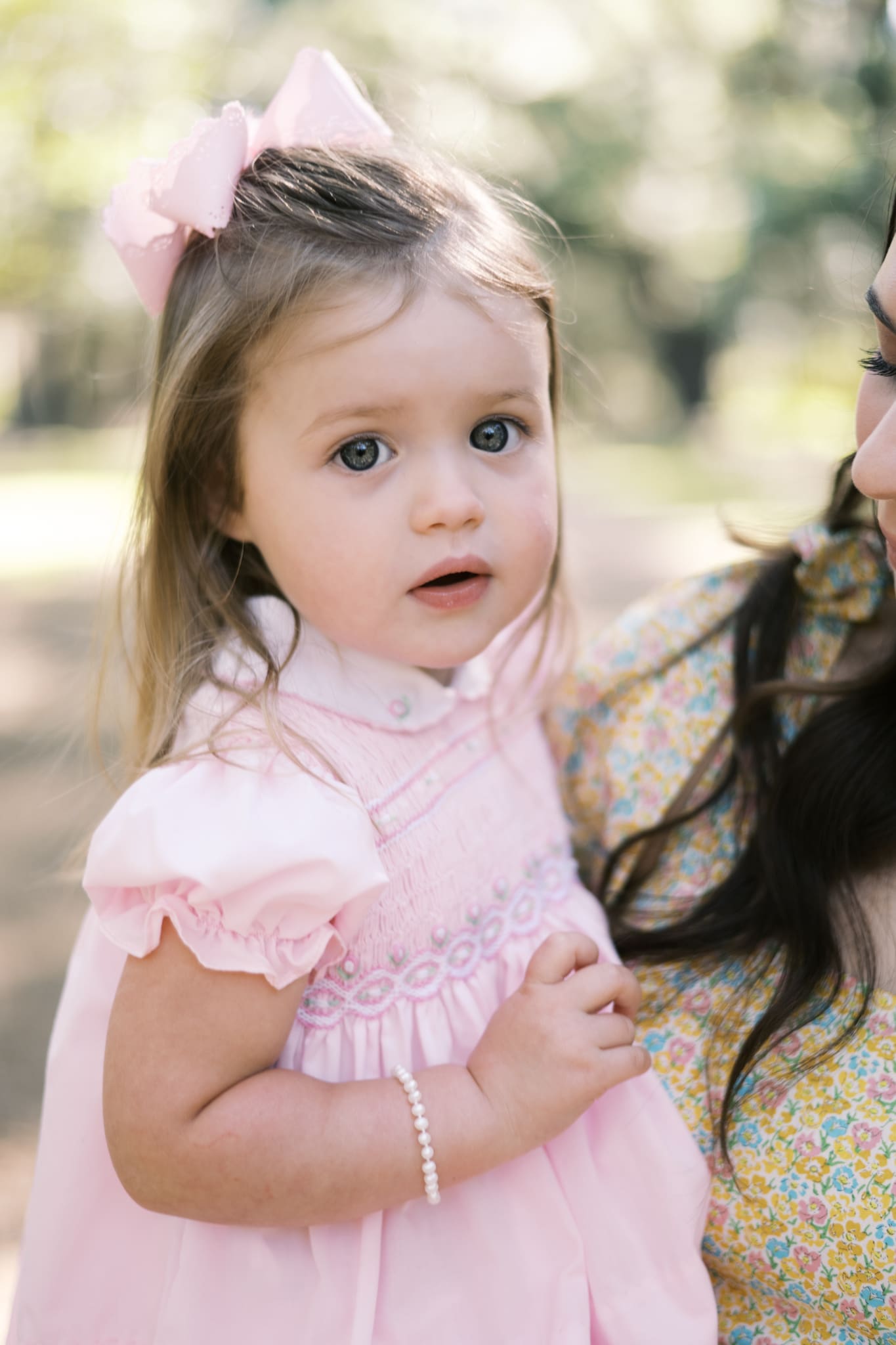 A close up image of a girl wearing a pink dress and bow while she looks at the camera