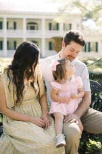 A family of three sits on a vintage style bench while the daughter looks lovingly at her father