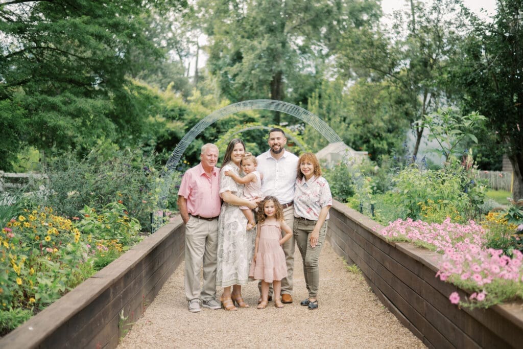A family of 6, including mom, dad, the kids and grandparents, stand together for an extended family portrait while smiling at the camera