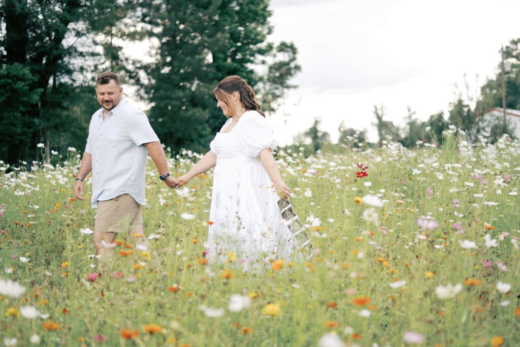 a mom and dad walk in a field of flowers while the mom holds the baby sonogram photo