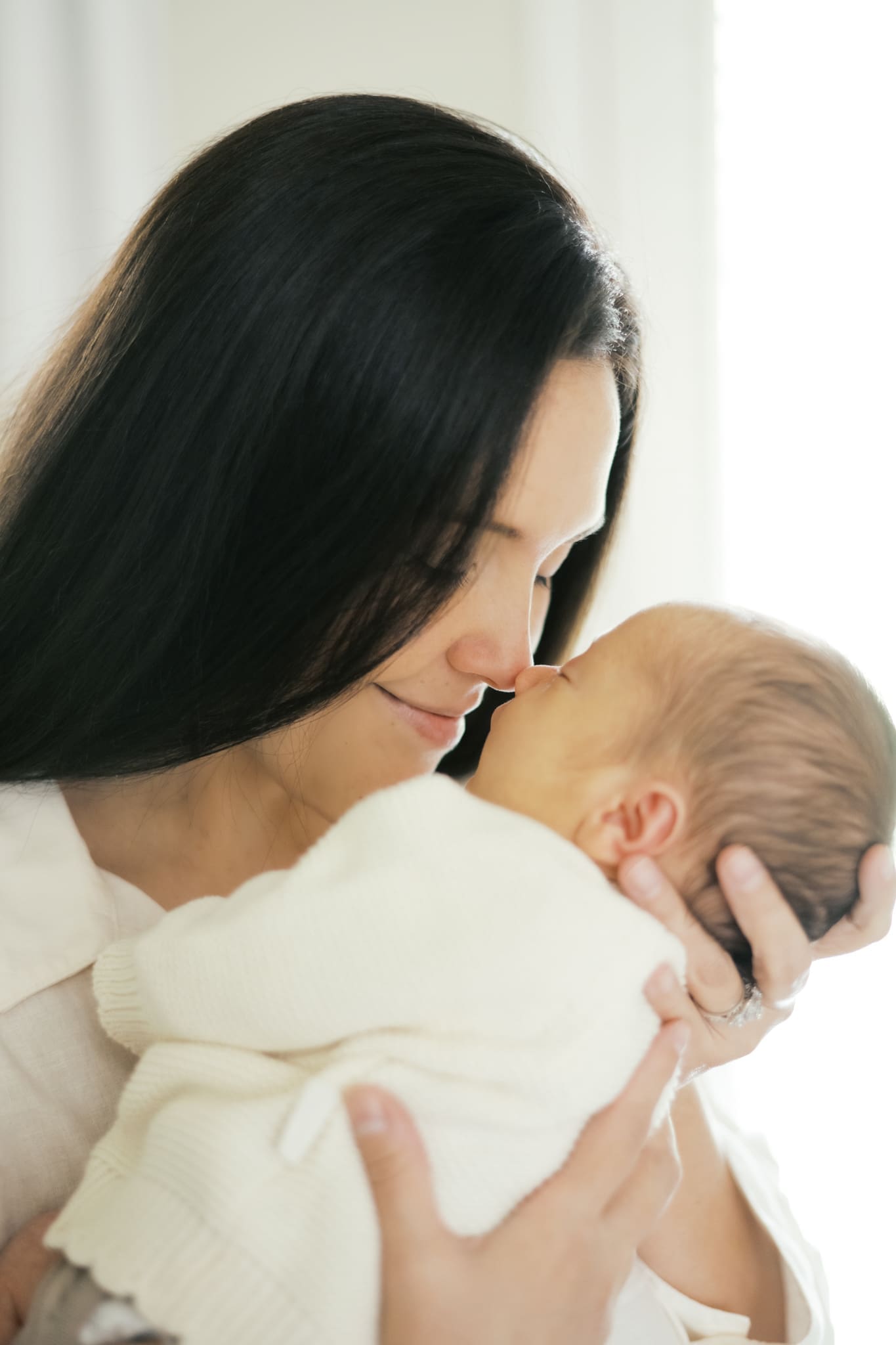 A close up image of a mother holding her newborn baby nose to nose as she smiles at the baby