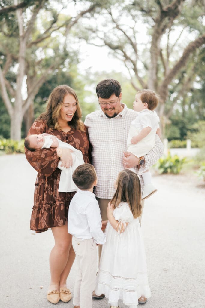 A family of six stand under oak trees and smile at each other