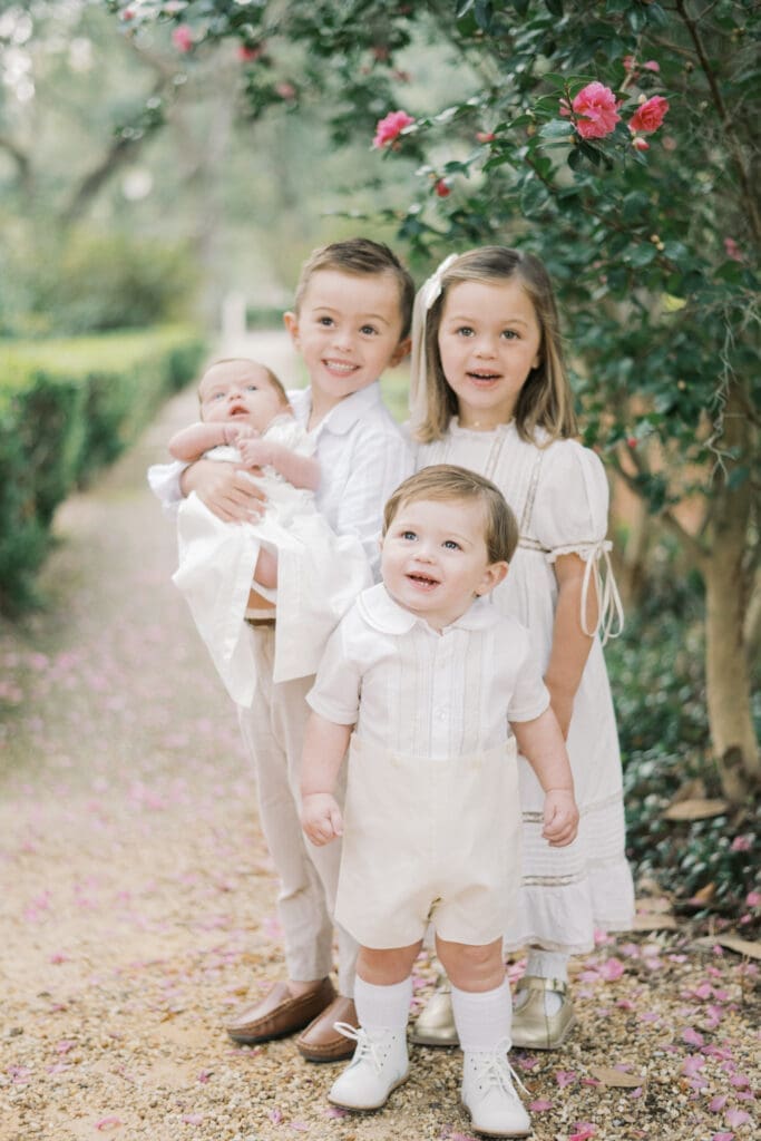 Four siblings stand under a camellia tree while the oldest brother holds his one month old brother