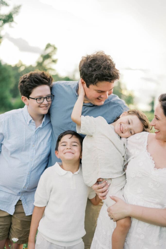 a family of five laugh and smile while the mom holds the toddler boy